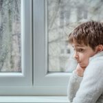 Sad child, looking out the window while grieving the loss of a pet.