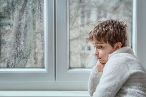 Sad child, looking out the window while grieving the loss of a pet.